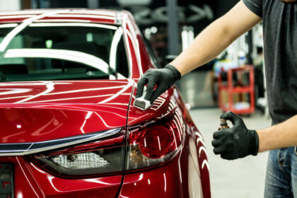 Aplikácia keramickej ochrany na červenú karosériu auta v dielni, technik nanáša ochranný náter na zadnú časť vozidla.